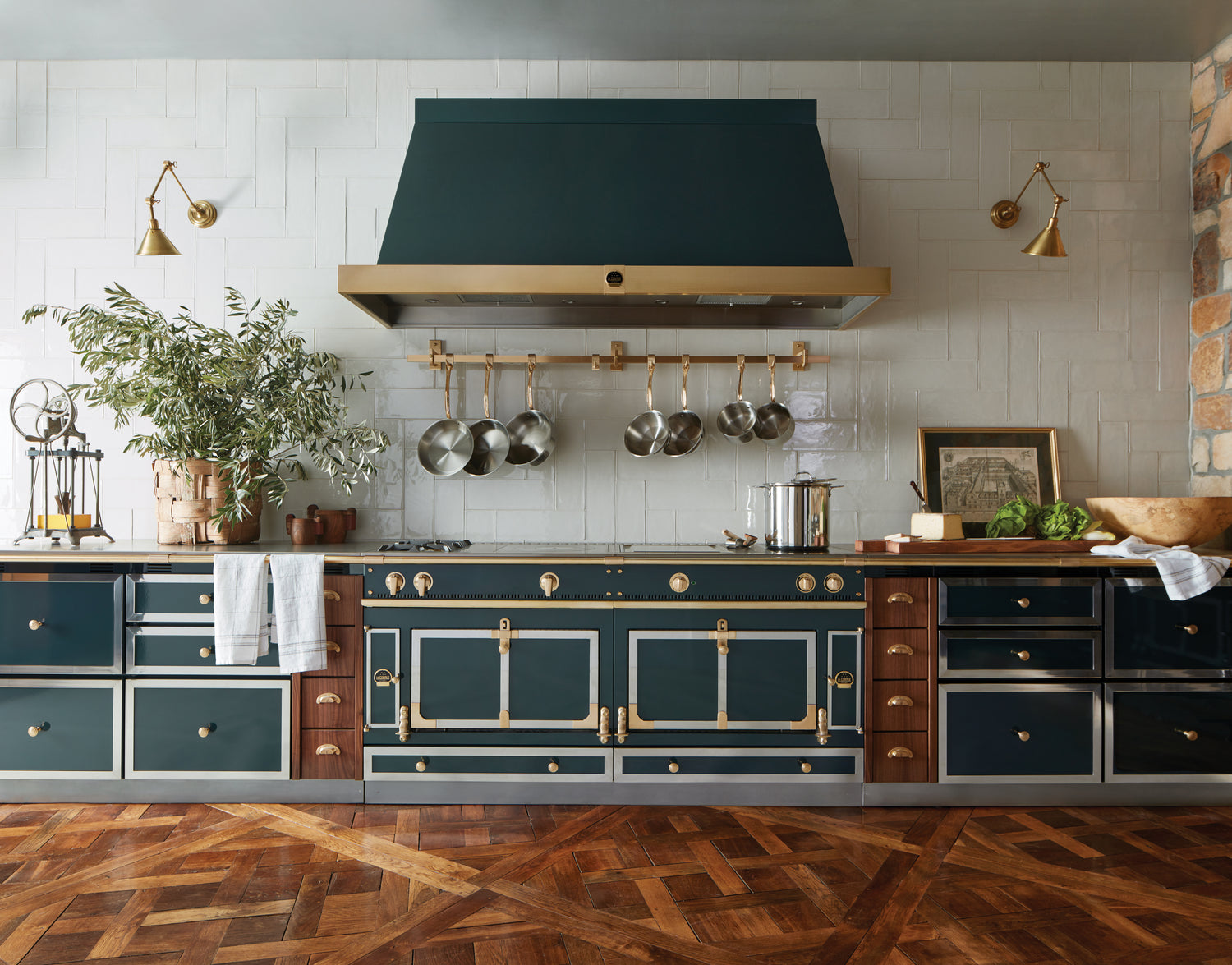 La Cornue green and brass range with matching hood in a luxury kitchen featuring white tile backsplash and herringbone wood floors.